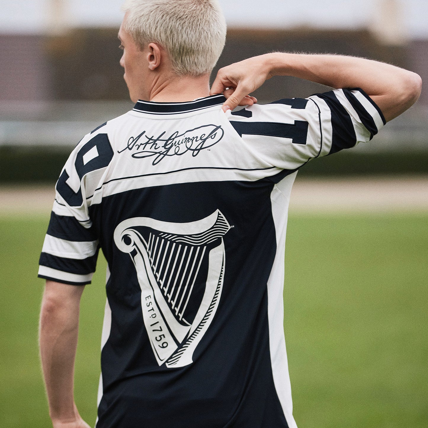 Back view of a man wearing a white and navy Guinness American football jersey with a large harp graphic on the back
