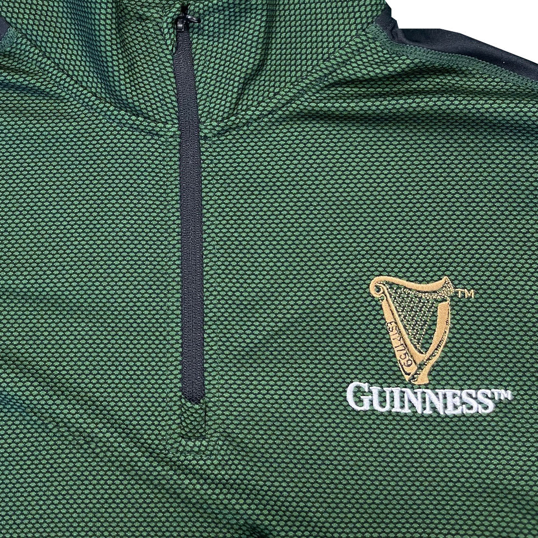 Close up of green textured fabric with a black zipper and Guinness crest embroidery on the chest