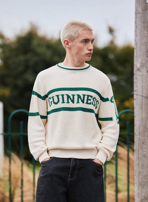 Model wearing cream Guinness Harp Sleeve knit sweater with green stripes outdoors.