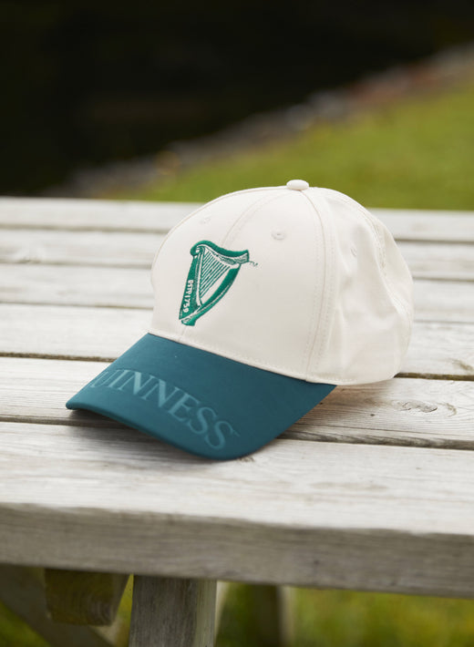 White and green baseball cap with harp logo on wooden table outdoors