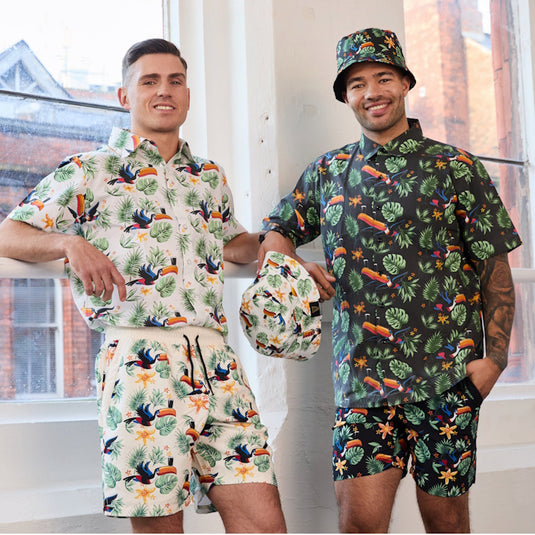 Two male models wear Guinness Toucan Hawaiian Print tropical shirts with matching shorts posing in a bright studio