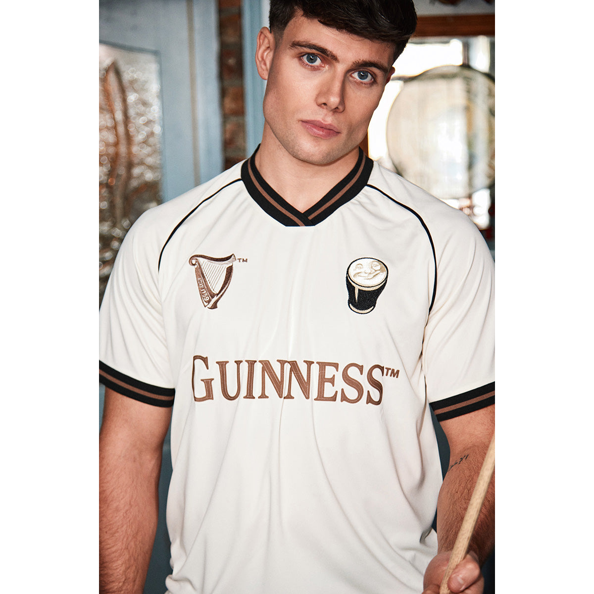 Male model wearing a cream Guinness jersey with brown trim and large GUINNESS lettering