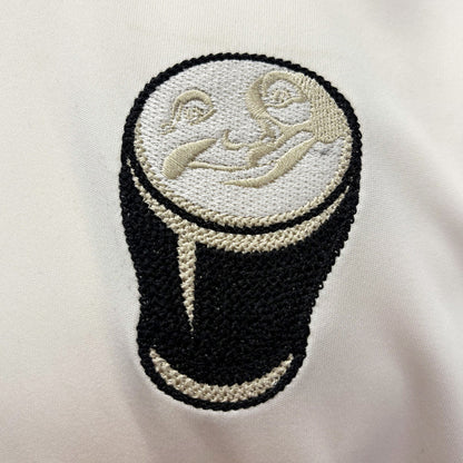 Close up of cream fabric showing an embroidered circular patch depicting a pint of beer.