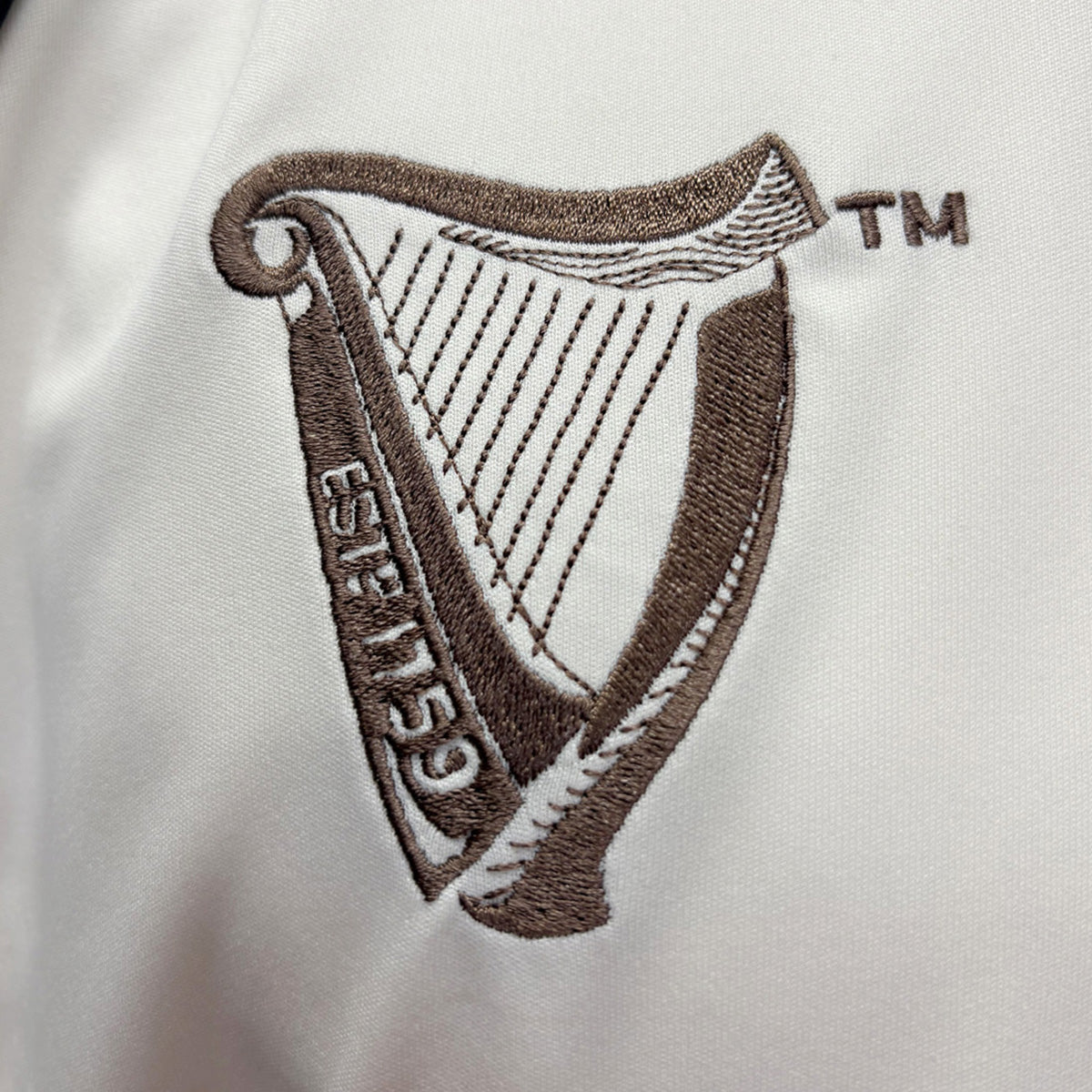 Brown embroidered Guinness harp crest on cream fabric jersey.