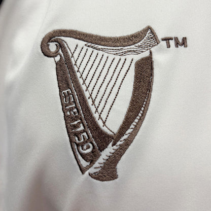 Brown embroidered Guinness harp crest on cream fabric jersey.