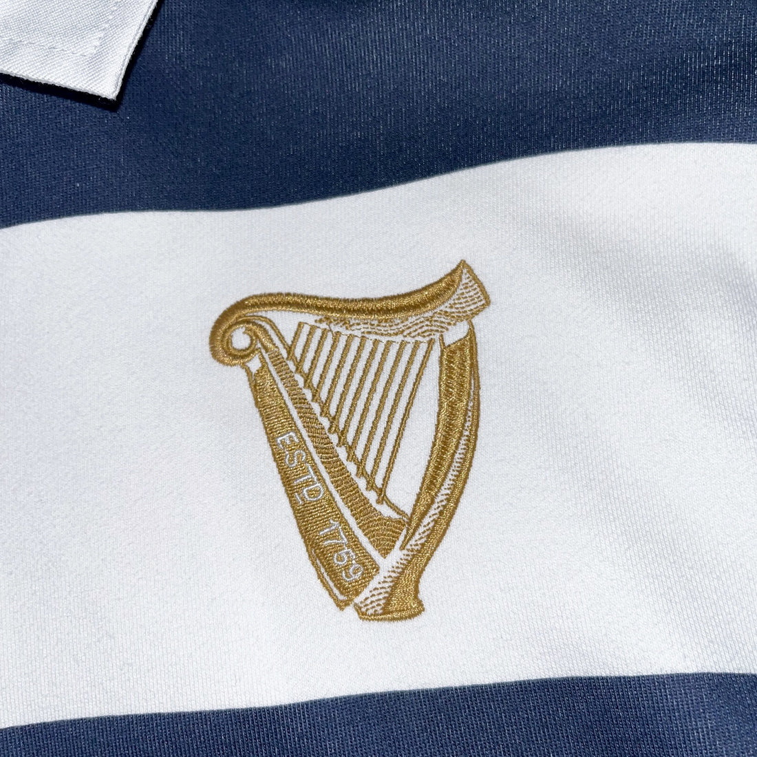 Gold harp crest embroidered on a white stripe of the navy and white rugby sweatshirt