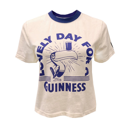 Cream cropped T shirt with bold blue Guinness graphic featuring a toucan and the phrase Lovely Day For Guinness