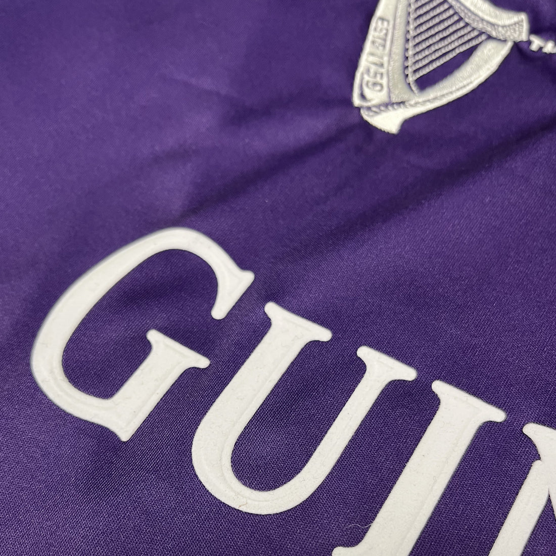 Close up of purple fabric with large white GUINNESS letters and a partial crest.
