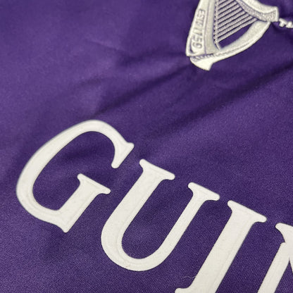 Close up of purple fabric with large white GUINNESS letters and a partial crest.