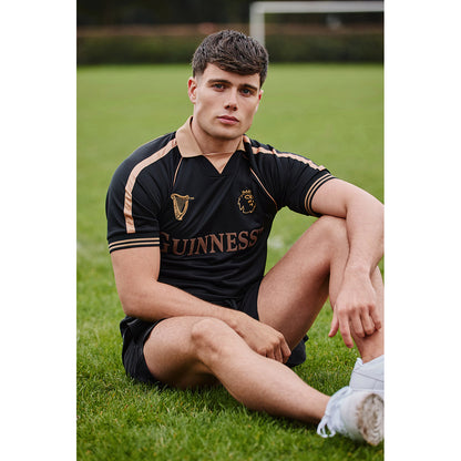 Man wearing Guinness Black and Brown Premier League football top with tan piping on a grassy field.