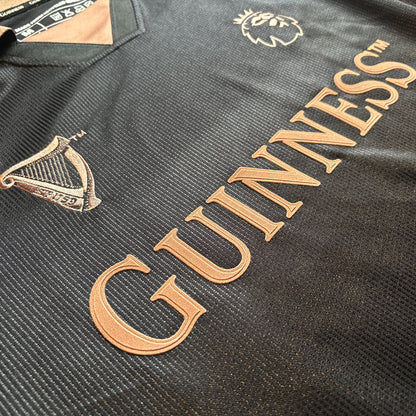 Close up of bronze embroidery on black fabric displaying the Guinness wordmark and crest details