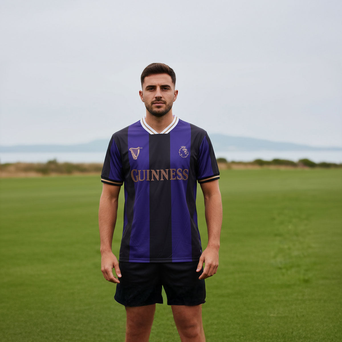 Man wearing Guinness black and purple striped Premier League football top outdoors on a grassy field