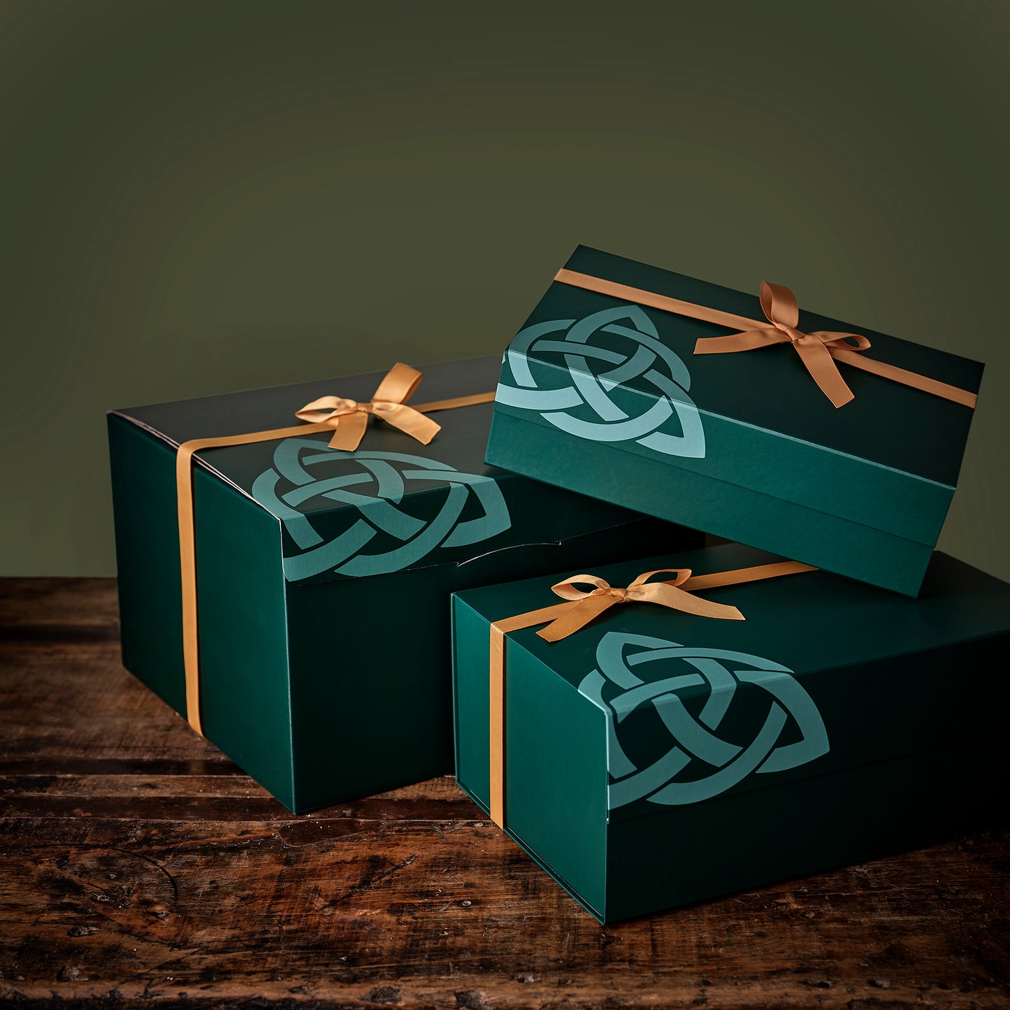 Dark green Enniskinn Wellness gift boxes tied with gold ribbons and Celtic knot patterns