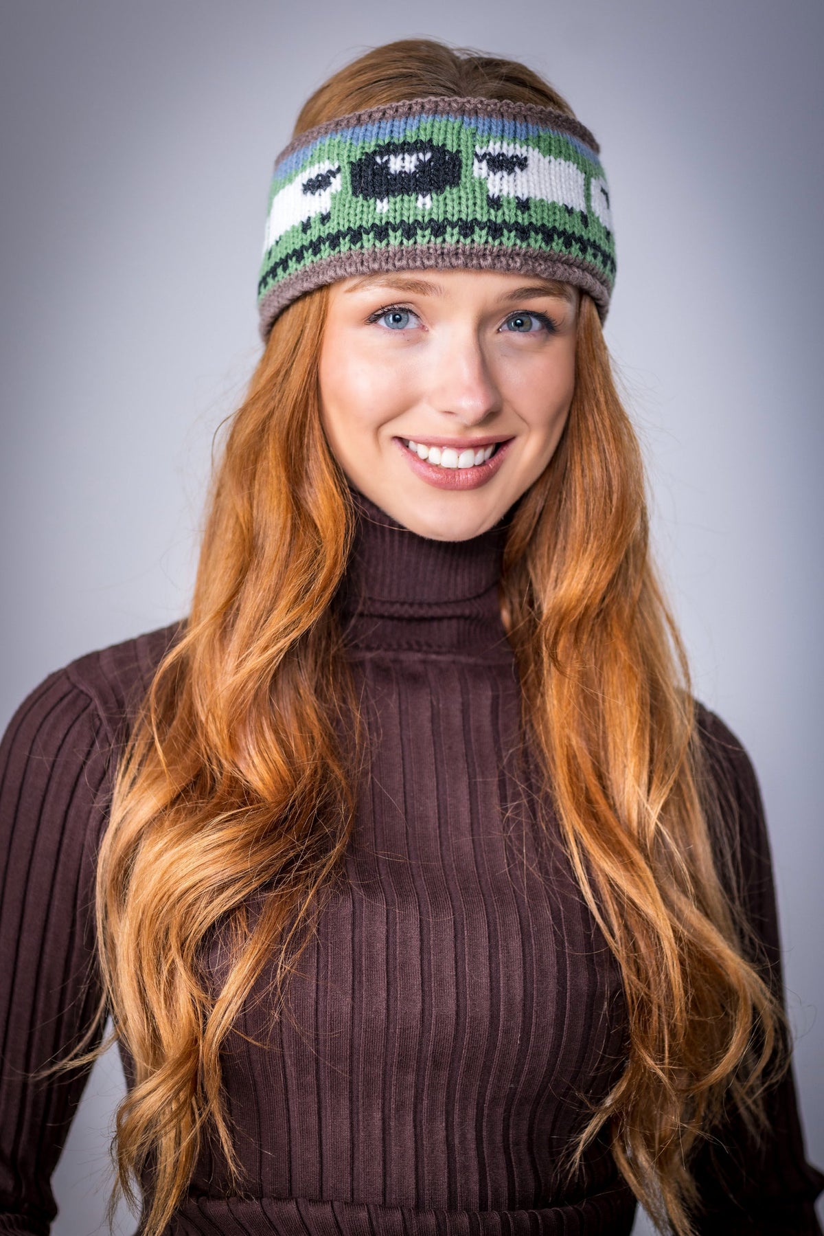 Smiling woman with long red hair wearing a knitted headband with sheep