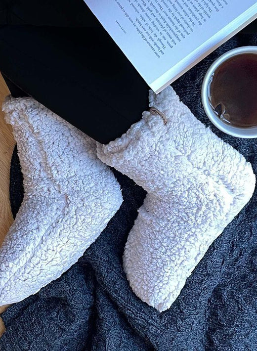 Person wearing white fuzzy slippers, reading a book, holding a cup of tea