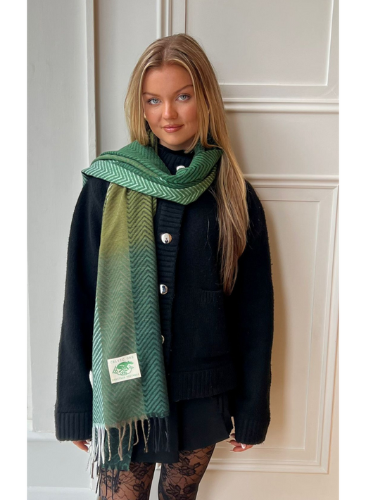 Model wearing a black coat with a green herringbone scarf wrapped around her neck.
