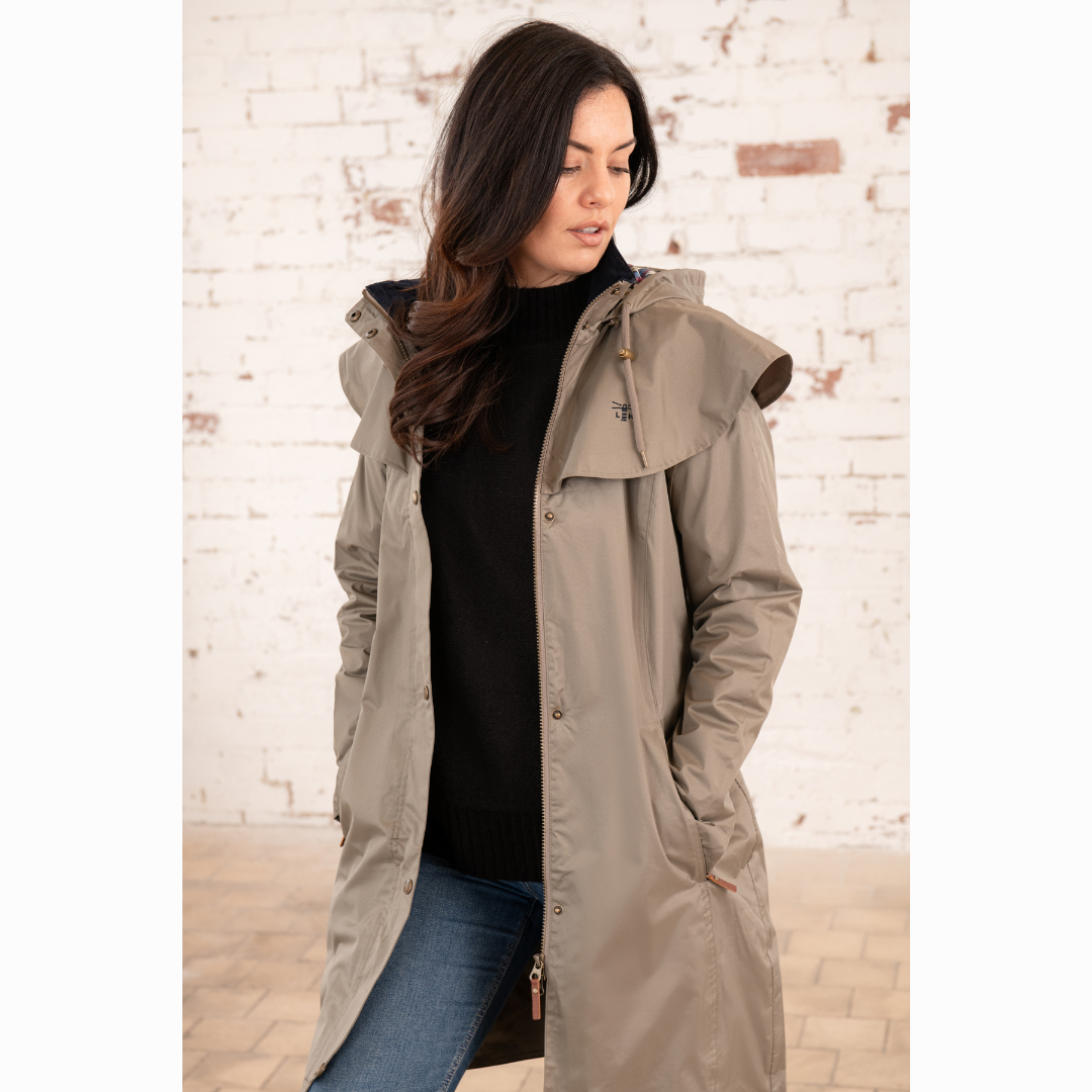 Model wearing taupe Ladies Outrider Waterproof Jacket with hood against a brick wall.