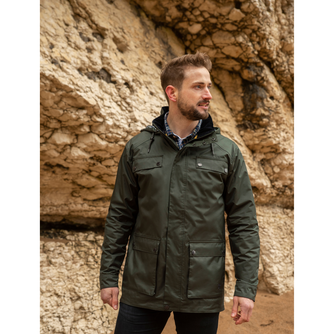 Man wearing a dark green Oxford waterproof jacket stands beside a rocky cliff.
