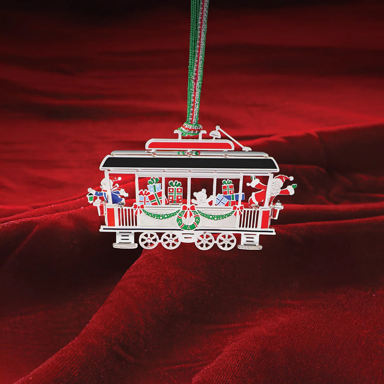 Red and white tram carriage Christmas tree ornament featuring wrapped gifts inside and greenery, hung by a green cord