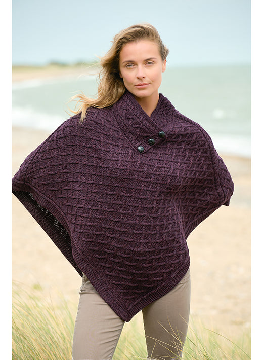 Woman on the beach wearing a deep plum merino poncho with a buttoned collar
