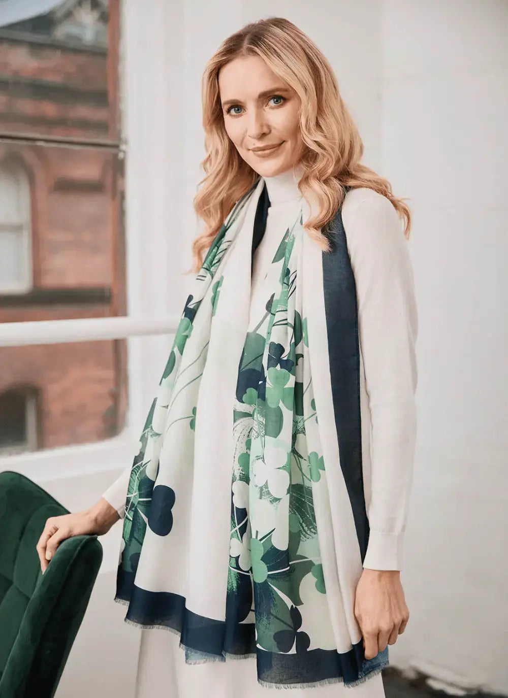 Profile of a model in a white outfit wearing the shamrock scarf draped over her shoulders with green and navy prints.