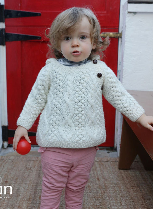 Toddler wearing a white knitted sweater holding a red ball indoors