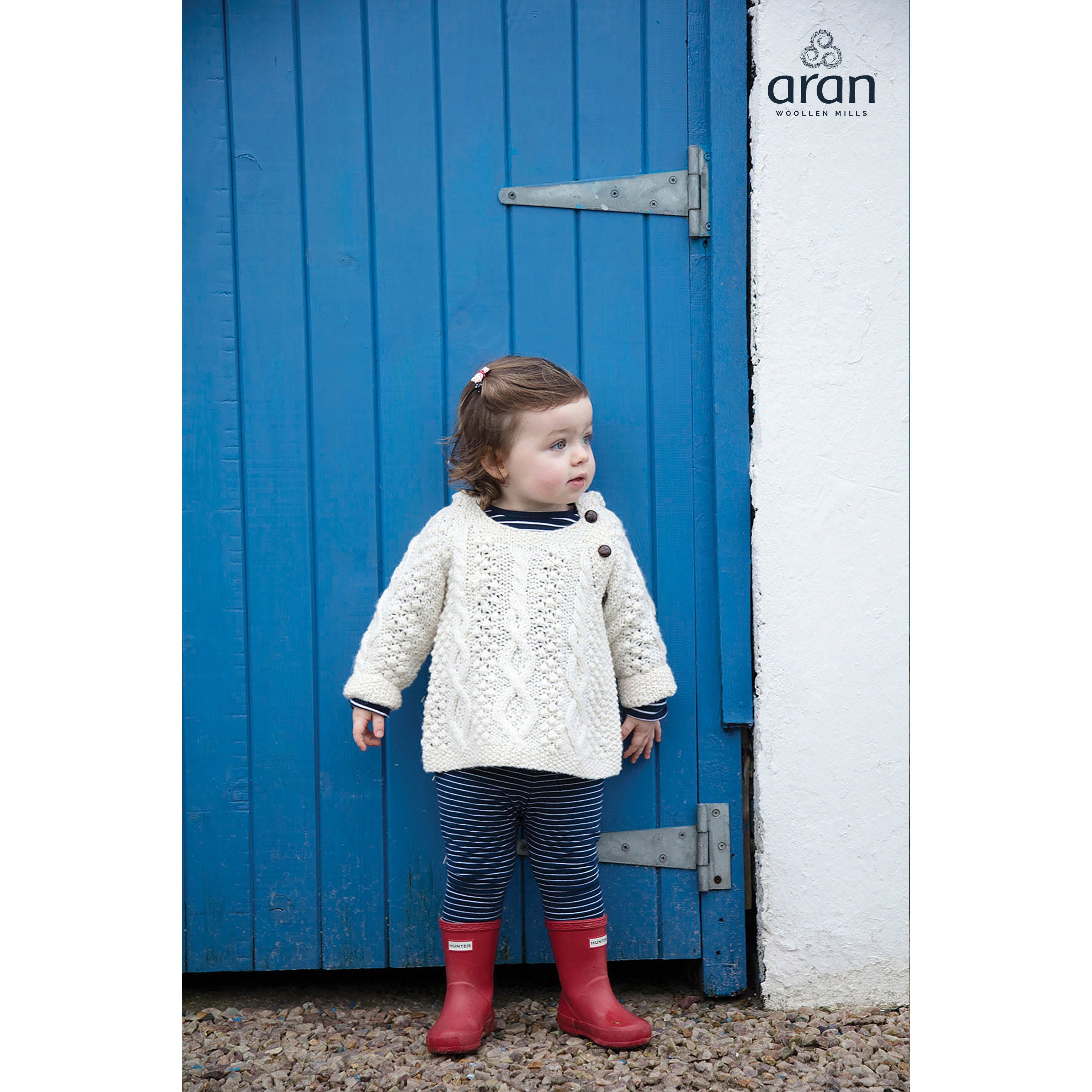 Toddler wearing knitted sweater and red boots standing by blue door