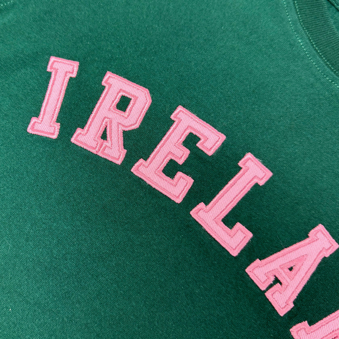 Close-up of pink embroidered IRELAND lettering on green fabric.