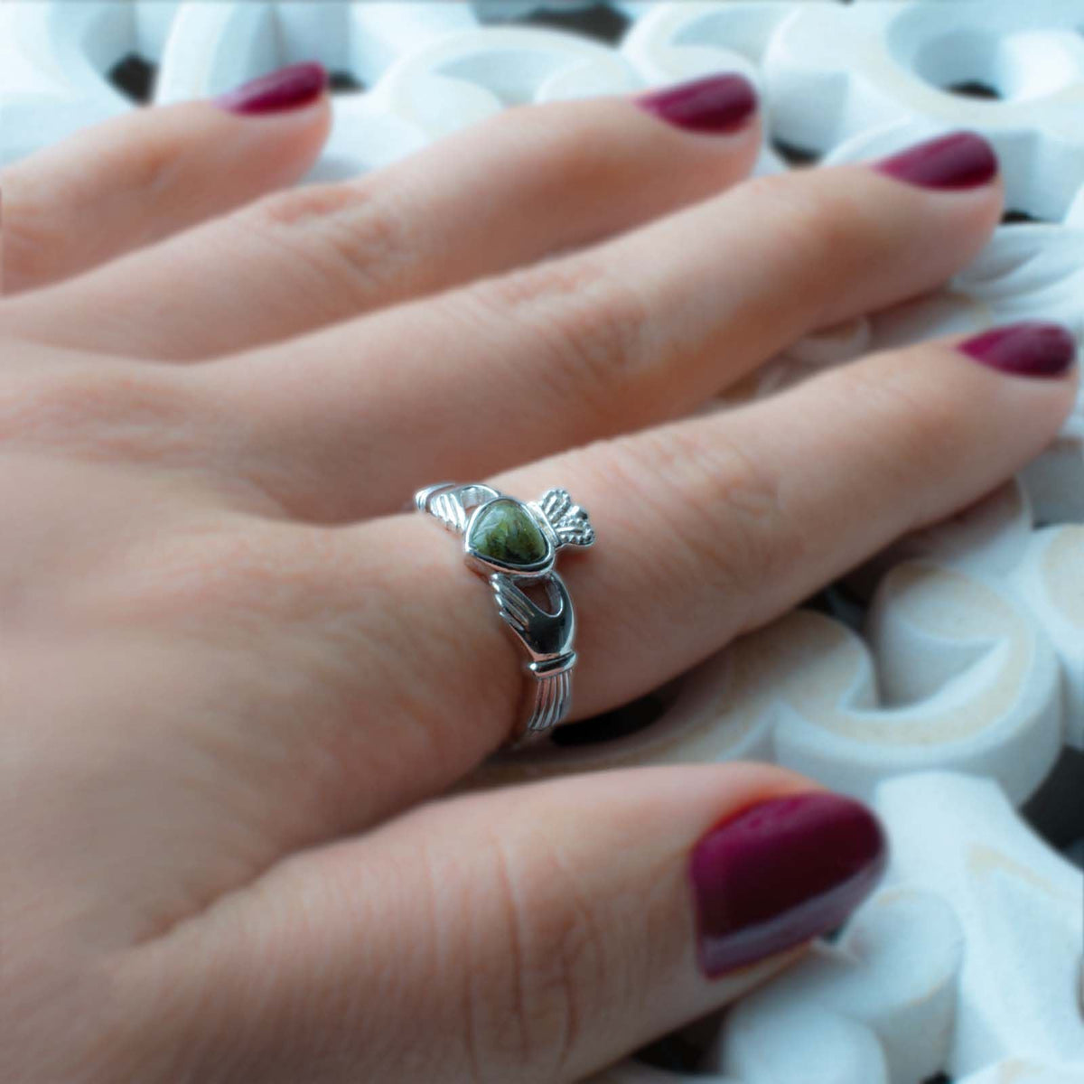 Close-up of silver Claddagh ring with green Connemara marble heart on a finger