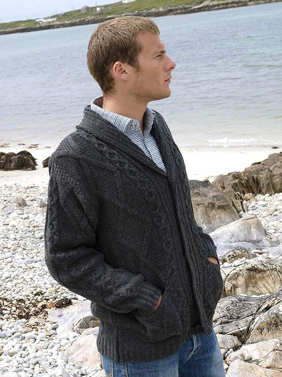 Man wearing dark knitted cardigan standing on rocky beach near water