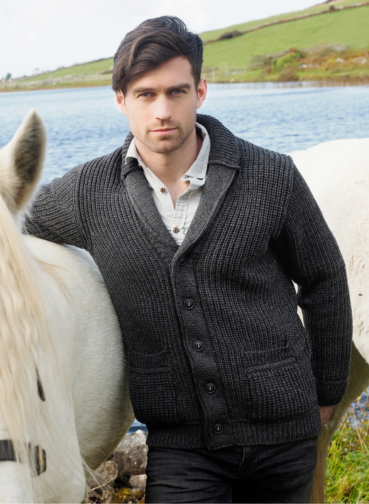 Male model wearing charcoal Aran knit cardigan outdoors beside a white horse by a lake