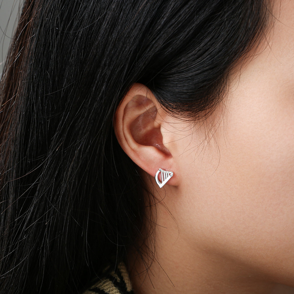 Close-up of ear with silver harp-shaped stud earring