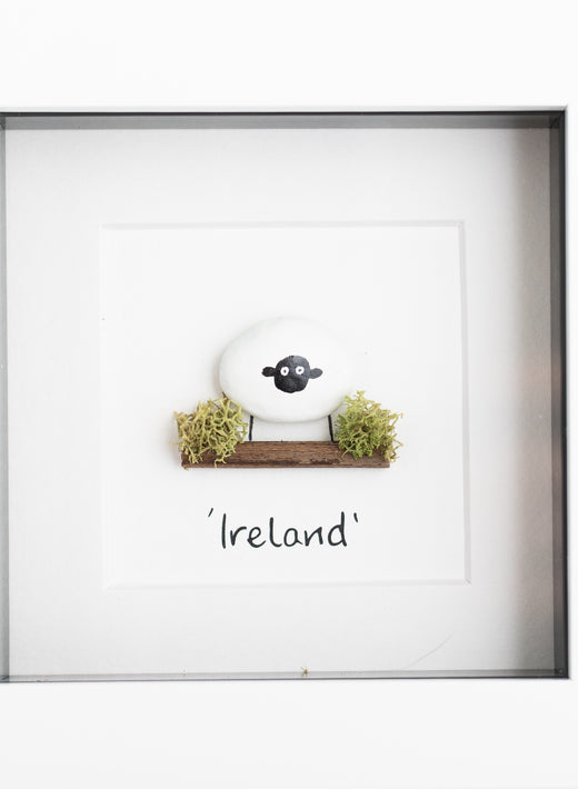 Pebble art print of a white sheep on a mossy log, framed in white with Ireland caption