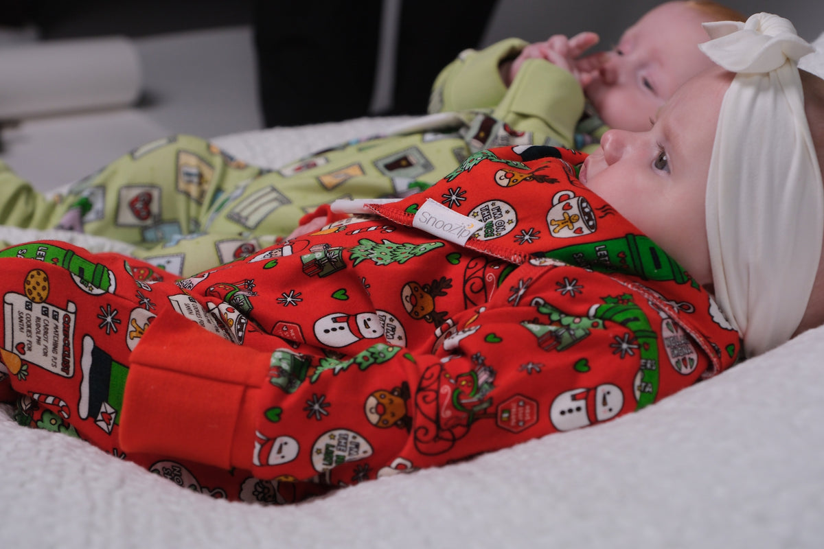 Baby wearing a red Kid's Signature Christmas Onesie with festive print lying on a soft white surface