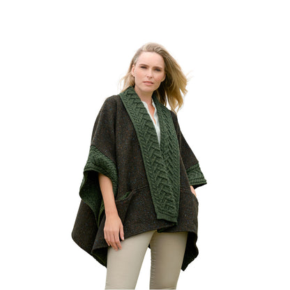 Woman wearing army green Donegal merino wool cape with chunky knit trim and oversized drape.