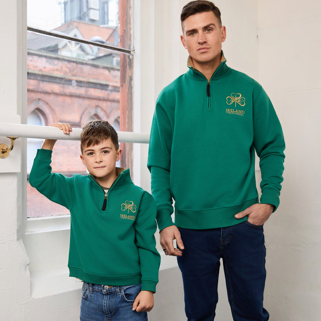 Adult and child in matching green Ireland Premium Quarter Zip Sweatshirts with gold chest logos pose indoors