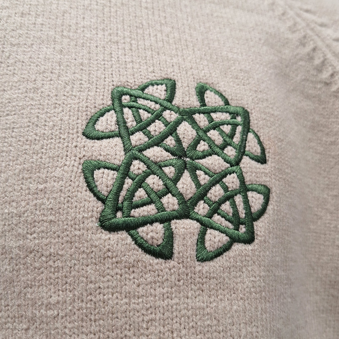 Close-up of green Celtic knot embroidery on beige knit fabric of the Celtic Knot Stone Crew Neck sweater