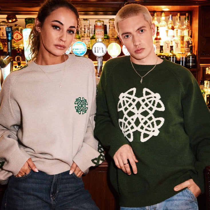 Two models wear Celtic Knot Stone crew neck sweaters in a bar; beige with green crest and a dark green version.