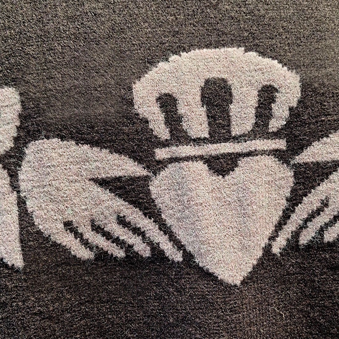 Detail of the gray heart motif with decorative elements on the black knit Claddagh sweater.