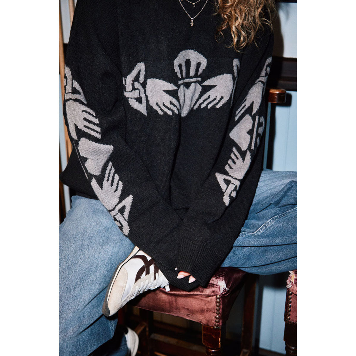 Close-up of the black knit Claddagh sweater showing a gray crest with crown and heart motif.