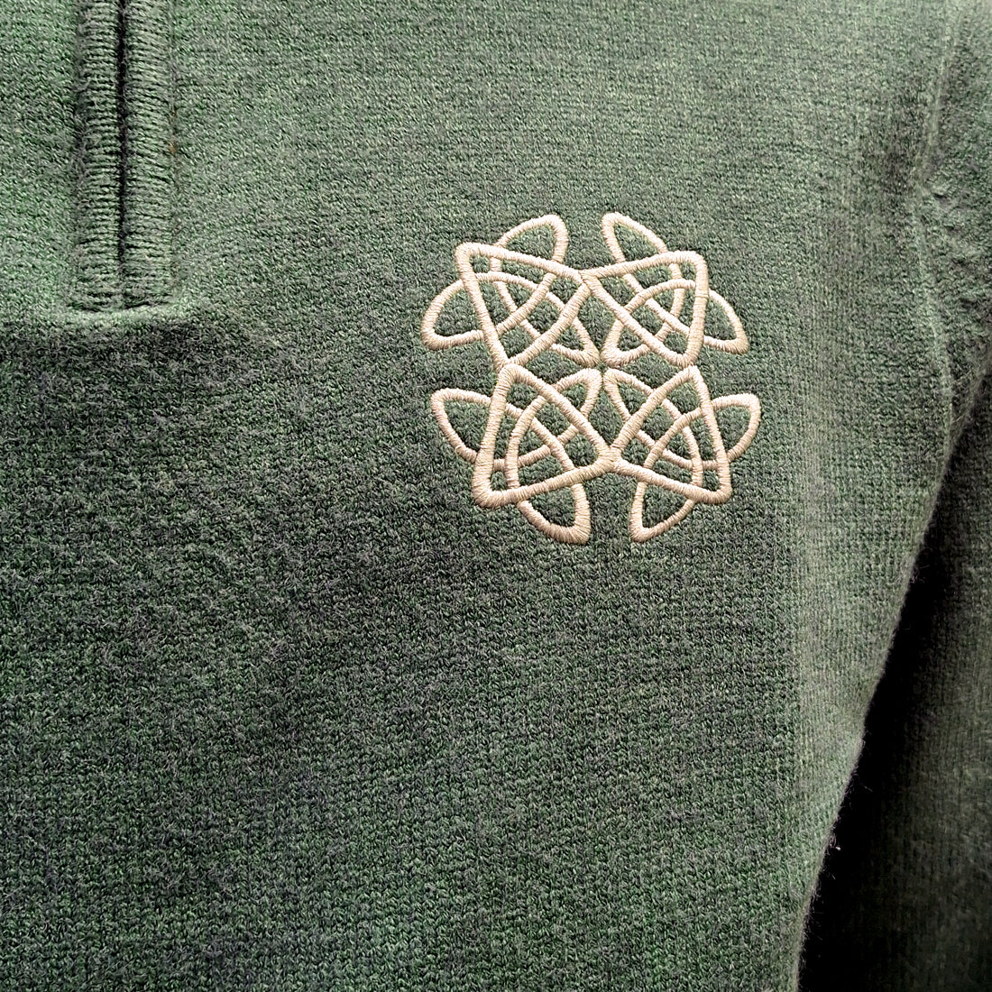Close-up of cream Celtic knot embroidery on sage green knit sweater.