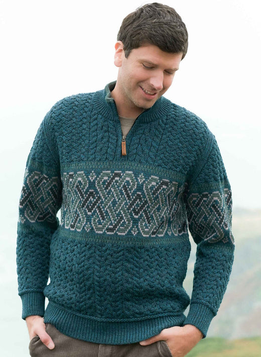Man wearing a teal half zip Celtic jacquard Peacock Aran sweater outdoors.