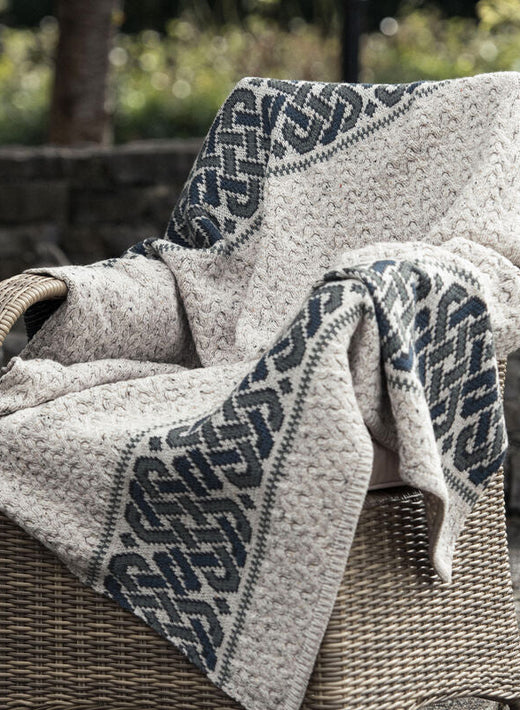 Woven beige and gray patterned blanket draped over wicker chair outdoors