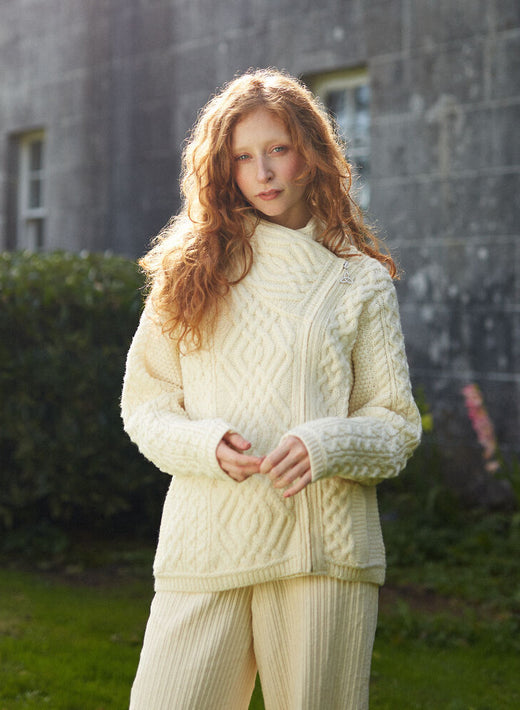 Young woman with curly red hair wearing cream knit sweater and pants outdoors