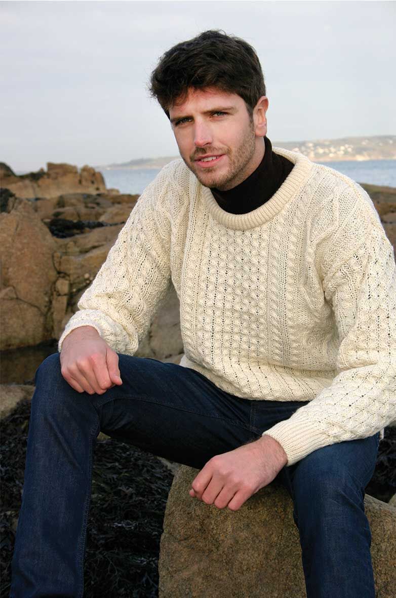Man wearing cream cable-knit sweater sitting on rock by the sea