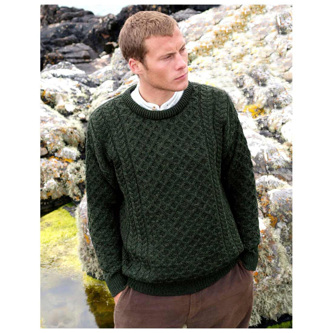 Man wearing a dark green Merino wool Aran crew neck sweater outdoors among rocks.