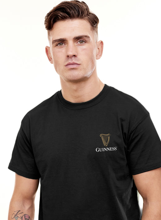 Male model wearing black Guinness Harp short sleeve T-shirt with gold logo on the left chest