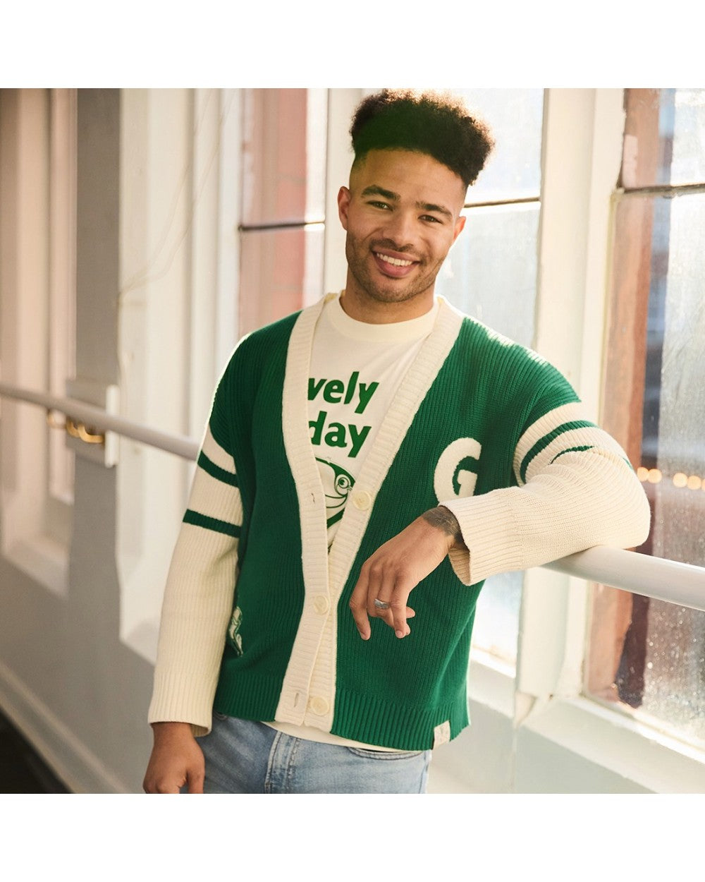 Male model wearing Guinness knitted green and cream cardigan over a white tee in a bright, airy setting.
