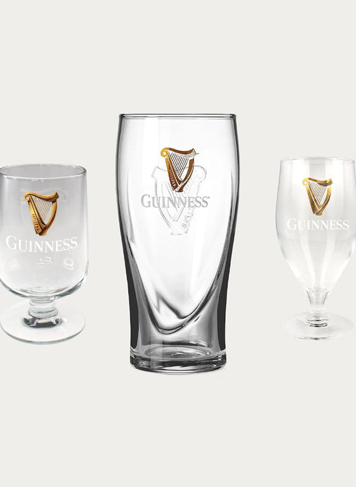 Assorted Guinness branded glassware including a tall pint glass centered among smaller glasses on a light background.