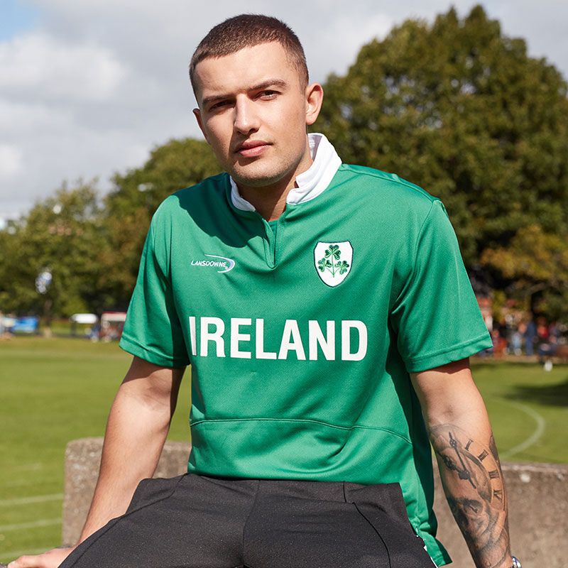 Man wearing green Ireland rugby top with shamrock crest posing outdoors.